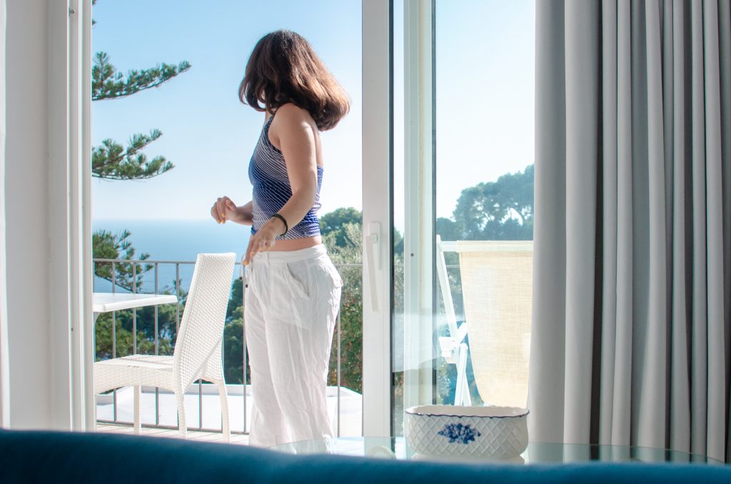 A Hotel Floridiana erkélyén Capri szigetén. Az erkélyről látszik a tenger. Én kék-fehér csíkos toppban és fehér len nadrágban.