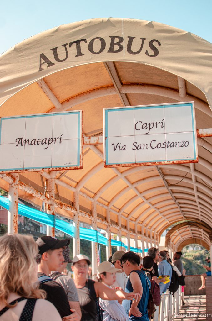A buszmegálló Caprin, ahhol a sorok felett kerámia táblák jelzik hol állj sorba. 2 sor van Capri és anacapri. Ponyvával fedett várakozó terület. "Autobus" felirattal